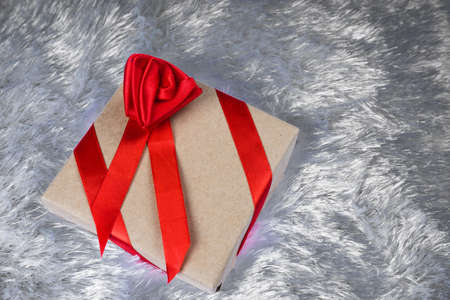 Gift box Packed in paper and tied with a red ribbon with a bow in the shape of a rose on a pillow fake fur.の写真素材