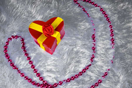 Gift box in the shape of a heart tied with a yellow ribbon with a bow in the shape of a rose is a...