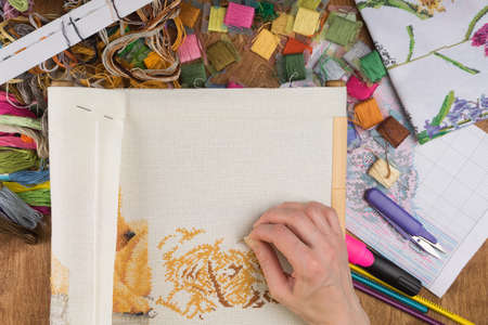 Girl sitting at a table where everything is necessary for embroidery, embroiders a big picture. Copy...