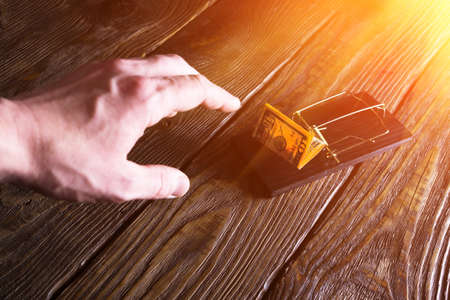 Man's hand stretch for a banknote which is bait in a mousetrapの写真素材