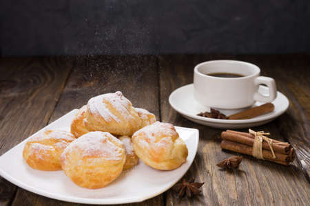 Delicious eclairs sprinkled with icing sugar, stand on a wooden table.