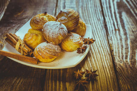 Delicious eclairs sprinkled with icing sugar, stand on a wooden table.