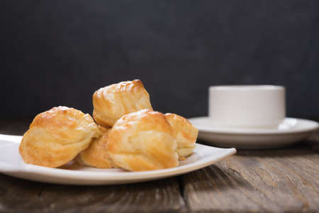 Delicious eclairs sprinkled with icing sugar, stand on a wooden table.