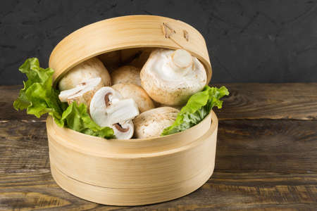 Round container with lettuce leaves and mushrooms on a table.の写真素材