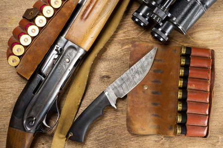 Hunting rifle and ammunition lie on wooden background.