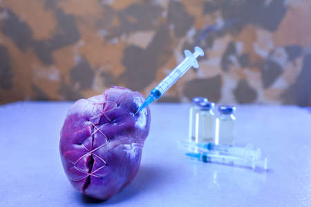 Heart punctured with a syringe and a group of medicines on the table. Horizontal composition.の写真素材