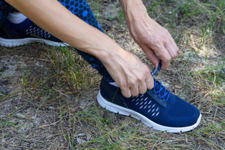 Young fitness woman runner tying shoelace on forest trail. Copy paste