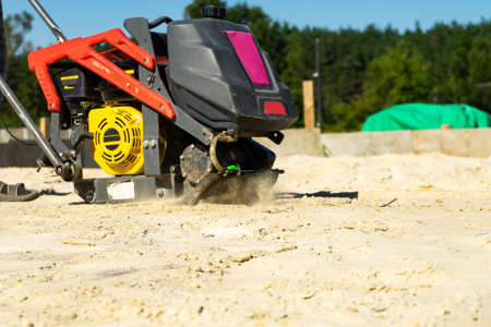 Builder with vibratory plates seals the base sand for pouring concrete. Copy pasre