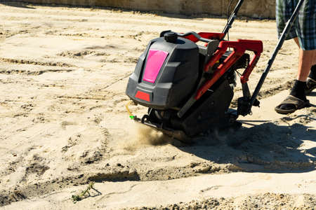Builder with vibratory plates seals the base sand for pouring concrete. Copy pasre
