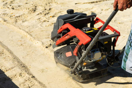 Builder with vibratory plates seals the base sand for pouring concrete.