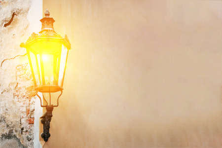 Ancient lantern on the textured wall shines with warm lightの写真素材
