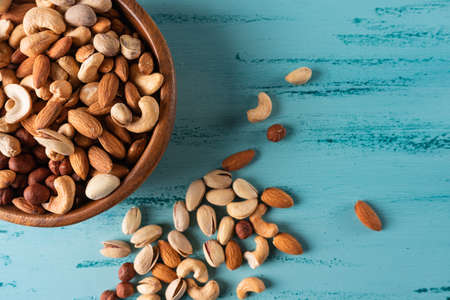 Assortment of nuts in wooden bowl on blue wooden table. Cashew, hazelnuts, almonds.の写真素材