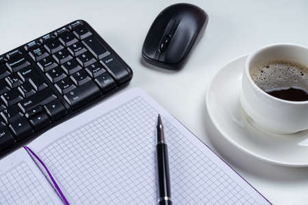 Office table desk. Workspace with blank note book, keyboard, office supplies and coffee cup on white background.の写真素材