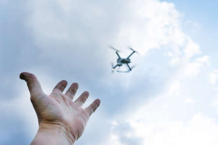 The mans hand reaches for the flying drone. The drone is out of focus.の写真素材