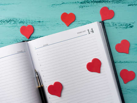 A Notepad and pen lie on a vintage wooden background. Red hearts around. Mock up Valentine dayの写真素材