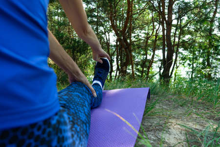 Fitness woman doing stretching exercises outdoors on grass. Girl doing hamstring leg stretching...