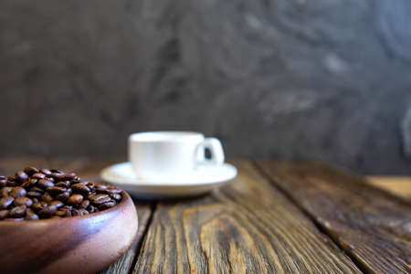 Coffee beans poured into a wooden bowl stands on a wooden table. White cupの写真素材