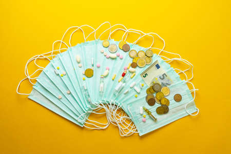 Sale of medical masks. Protective medical mask and different types of pills next to money on yellow background. Coronavirus concept. 2019 nCoV.の写真素材