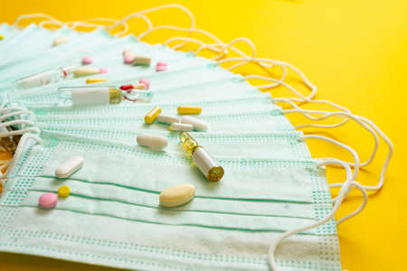 Protective medical mask and different types of pills on yellow background.の写真素材