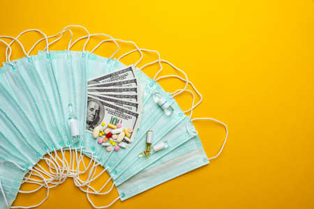 Sale of medical masks. Protective medical mask and different types of pills next to money on yellow background. Coronavirus concept. 2019 nCoV.の写真素材