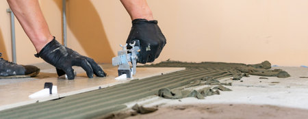 Workers are using plastic clamps and wedges to leveling the ceramic tile on the floor. Tile leveling system. Banner.の写真素材