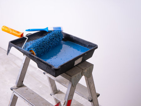 Cuvette for rollers with a roller and brush filled with blue paint stands on a stepladder.