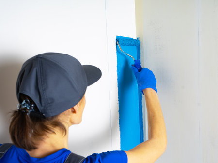 Female painter painting a white wall with a roller in blue color renovations or construction concept..の写真素材