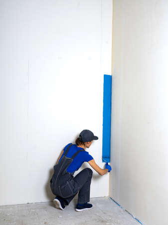 Female painter painting a white wall with a roller in blue color renovations or construction concept.の写真素材