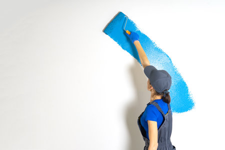 Female painter painting a white wall with a roller in blue color renovations or construction conceptの写真素材