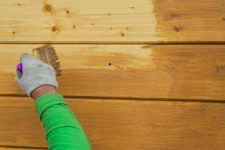 A worker's hand in a glove, painting a wooden house. Covering a wooden house with a protective compound.の写真素材