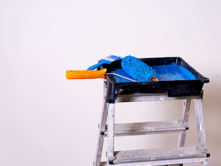 Cuvette for rollers with a roller and brush filled with blue paint stands on a stepladderの写真素材