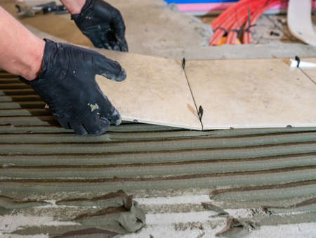 Skilled worker installing the ceramic tiles on the floor Worker making flooring on the construction site of the new apartmentの写真素材