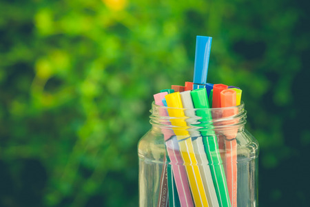Various color pen in glass bottle on concrete floor with green bush background in vintage style. (Selective focus)の写真素材