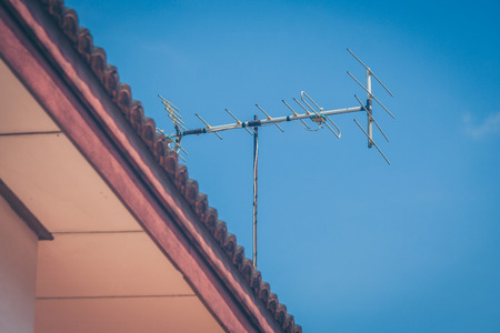 TV antenna on roof of house with blue sky background in vintage style.の写真素材