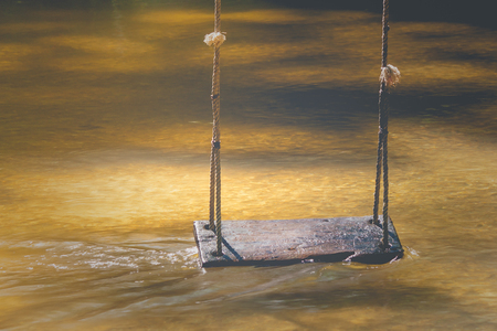 Relaxation Concept : Wooden swing hanging on tree above the water stream at outside resort in...
