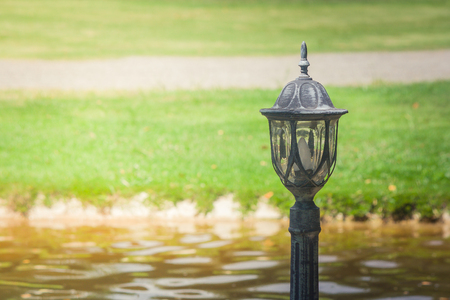 Close up old metal street lamp setting on concrete floor beside walkway on the road and river in vintage style.の写真素材