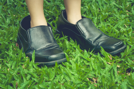 Legs of cute girl wearing black business shoes and standing on green grass in vintage style.の写真素材