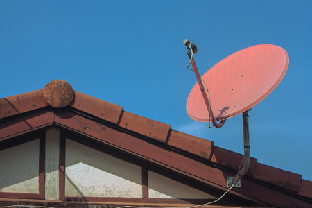 Digital satellite television receiving dish setting on top of house roof with blue sky in the background.の写真素材