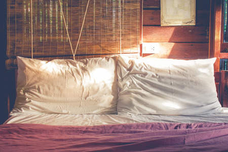 Close up two white crumpled pillow on bed with sunlight radiated from right hand of the bed room in morning time at countryside in vintage style. (Selective focus)の写真素材