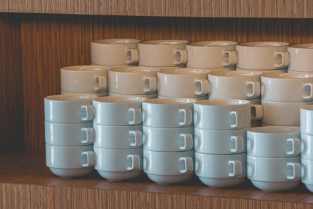 Close up stack of clean white coffee mug put on wooden shelf for breakfast preparation in the morning. (Selective focus)の写真素材