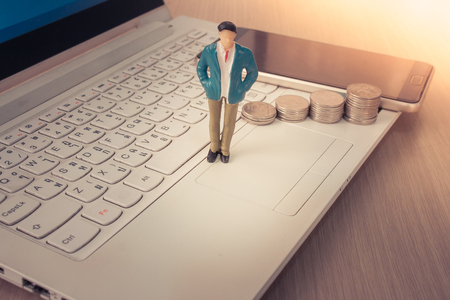 Business and Financial Concept : Business man standing on laptop with stack of silver coins and smartphone in the background. (Selective focus)の写真素材