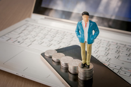 Business and Financial Concept : Business man standing on top of stack of silver coins and smartphone with laptop in the background. (Selective focus)の写真素材