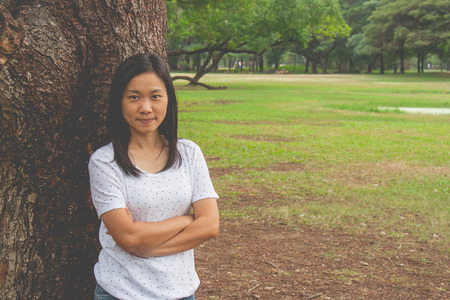 Woman wearing white t-shirt, she standing on green grass in the park and smiling.の写真素材