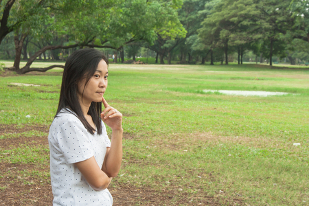 Woman wearing white t-shirt and standing on green grass in the park, she thinking something.の写真素材