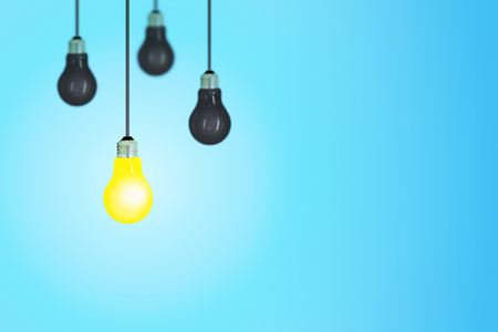 Business Idea Concept : One yellow light bulb of others black light bulb hanging from ceiling with blue background.の写真素材