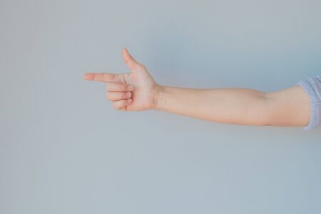 Hand of female gesturing in gun shape or gesture of single pointing finger with gray background.