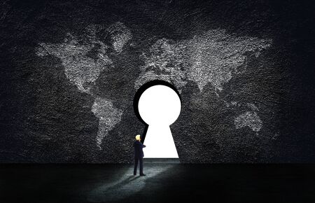 Business Success Concept : Businessman standing on concrete floor and looking at key hole on world map wall.の写真素材