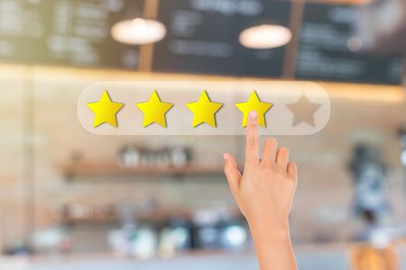 Customer Feedback Concept : Hand pressing one yellow star for giving best service ranking with blurred image of front view of cafe restaurant or coffee shop in background.の写真素材