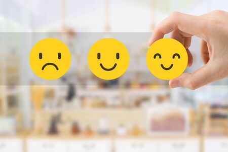 Customer Feedback Concept : Hand choosing smile emotion icons for giving best service ranking with blurred front view of cafe restaurant or coffee shop in the hotel.の写真素材