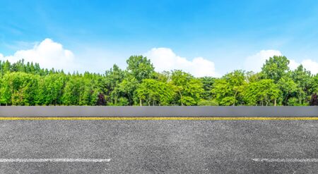Side view of Asphalt straight street roadway of lanes with lines and green trees with blue sky in background.の写真素材